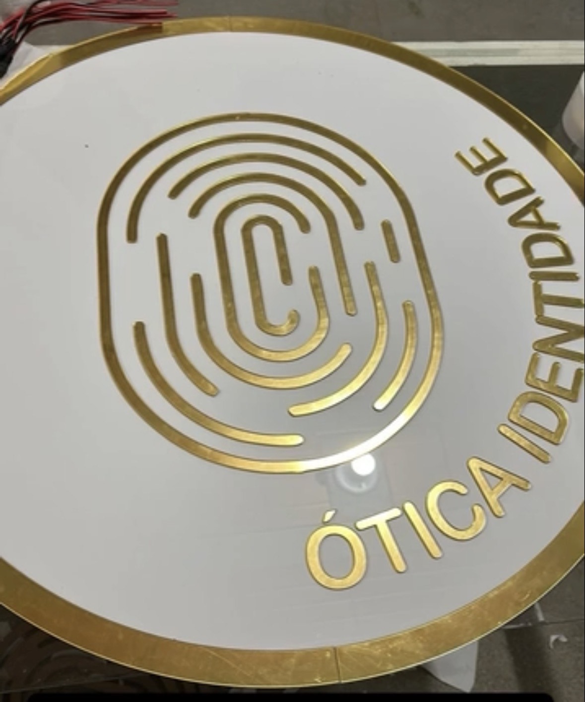 Placa redonda branca e dourada Ótica Identidade